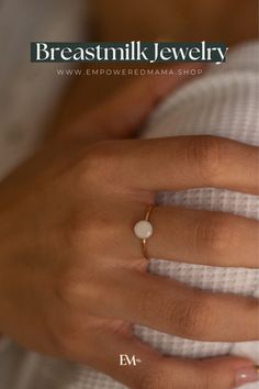 a woman's hand wearing a gold ring with a white pearl on the middle