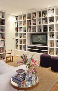 a living room filled with lots of white furniture and bookshelves next to a flat screen tv