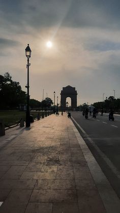 the sun shines brightly in front of an arch and street light on a cloudy day