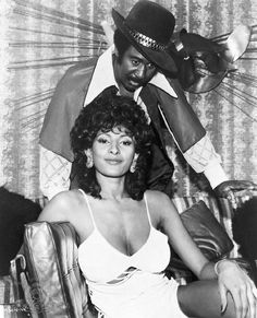 an old black and white photo of a woman sitting on a chair next to a man in a cowboy hat