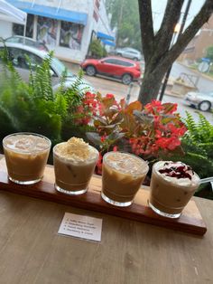 three drinks are sitting on a wooden tray in front of a window with cars outside