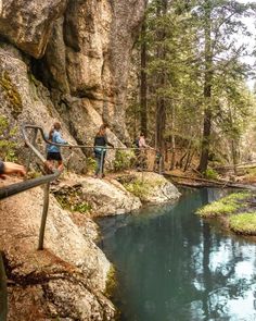 three people are walking up the stairs near a stream in the woods with rocks and trees