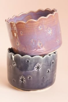 three ceramic bowls sitting side by side on a pink tableclothed surface, one with silver stars and the other has purple glaze