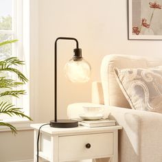 a table lamp sitting on top of a white table next to a couch and potted plant