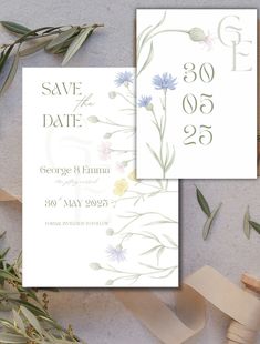 two wedding cards with flowers and greenery on them, next to some wooden pegs