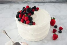 a cake with white frosting and fresh berries on top, next to a spoon