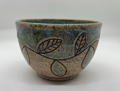 a blue and brown bowl with leaves on the inside is sitting on a white surface