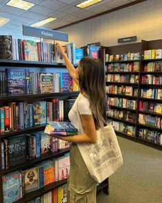 a woman is picking up some books from the shelves in a book store and pointing at them