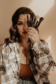 a woman holding up brushes to her face with one hand and the other in front of her face