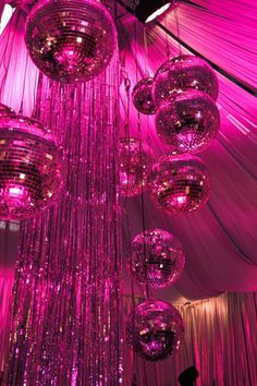 disco ball chandelier hanging from the ceiling in a tent with pink lights and draping