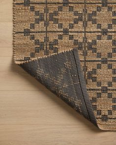 a close up of a rug on a wooden floor with a black and tan pattern