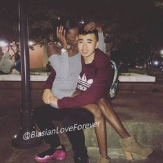 two people sitting next to each other on a street corner at night with their arms around each other