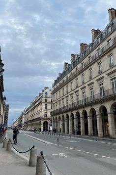 people are riding bicycles down the street in front of some old buildings on a cloudy day