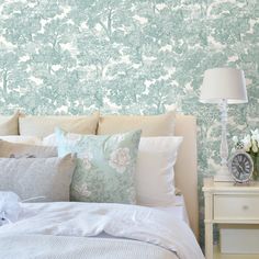 a bed with white pillows and green wallpaper next to a lamp on a nightstand