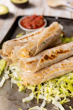 three burritos on a tray with lettuce and salsa in the background