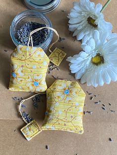 three small yellow bags sitting on top of a table next to some flowers and seeds