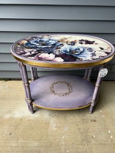 a table with flowers painted on the top and purple bottom, sitting in front of a house