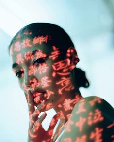 a woman with chinese writing projected on her face and hands in front of her face