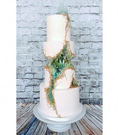 a three tiered white cake with green plants on top and brick wall in the background