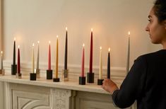 a woman standing in front of a mantle with candles lined up on top of it