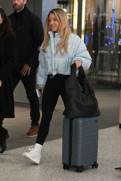 the woman is walking with her luggage through the airport terminal while another man looks on