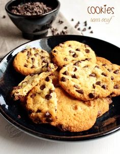 chocolate chip cookies on a black plate next to a bowl of cocoa chips and a glass of milk