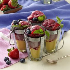 three cups filled with ice cream and fruit on top of a table next to spoons