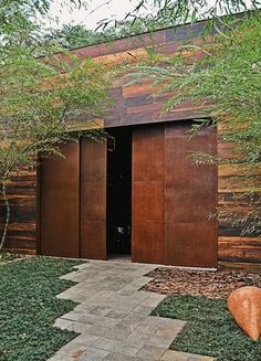 a wooden building with two brown doors on the outside and green grass in front of it