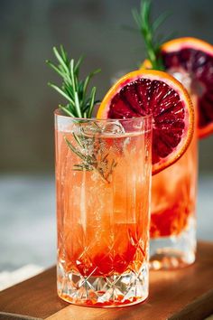 two grapefruit cocktails with rosemary garnish sit on a cutting board