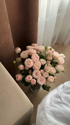 a vase filled with pink roses sitting on top of a wooden floor next to a window