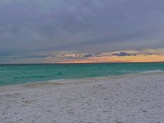 a person walking on the beach with a surfboard under their arm as the sun sets