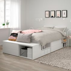 a white bed sitting next to a window on top of a wooden floor