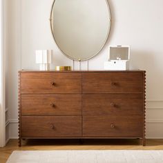 a wooden dresser with a round mirror above it and a white rug on the floor