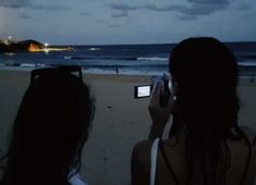 two people are taking pictures at the beach with their cell phones in front of them