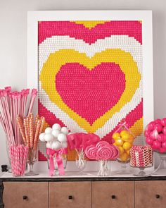 a table topped with candy and lollipops in front of a large heart