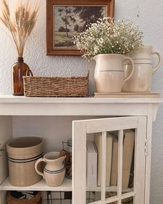 a shelf filled with dishes and vases on top of a white cabinet next to a painting