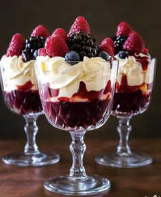 three desserts with berries and whipped cream in small glass dishes on a wooden table