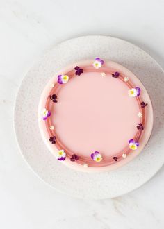 a pink cake with purple and yellow flowers on it sitting on a white platter