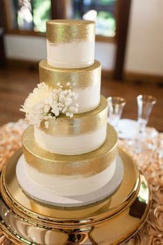 a three tiered wedding cake with white flowers on the top and gold trimmings