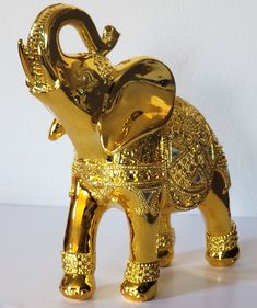 an elephant made out of gold foil on a white surface with a wall in the background