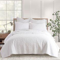 a white bed in a bedroom next to a window with a potted plant on it