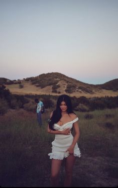 a woman in a white dress standing on top of a grass covered field next to a man