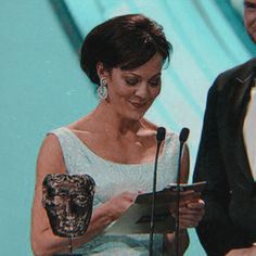 a man and woman standing next to each other in front of microphones holding an award