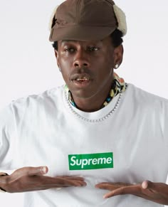 a man wearing a supreme t - shirt and hat with his hands out in front of him