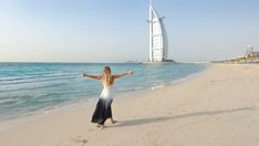 a woman standing on top of a sandy beach next to the ocean with a tall building in the background