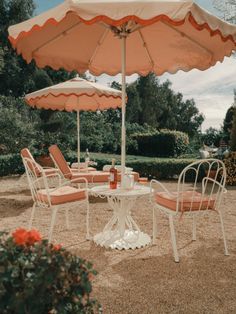 an outdoor table with chairs and umbrella in the middle of a garden area that looks like it has been set up for lunch