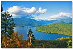 a lake surrounded by mountains and trees with clouds in the sky over it's water