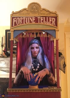 a woman dressed as fortune teller sitting in front of a blue vase with her hands on it