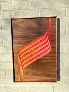 a wooden wall hanging on the side of a brick building with an orange and red design