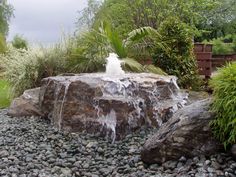 a large rock with water coming out of it in the middle of a garden area